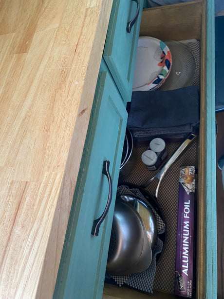 Inside an **rv rental** kitchen drawer: organized plates, towels, spices, and aluminum foil on a checkered liner.