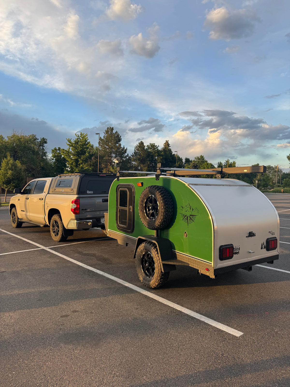 Adventure-ready RV rental: Tan pickup truck with camper shell towing a green teardrop trailer, perfect for camping adventures under a cloudy sky.