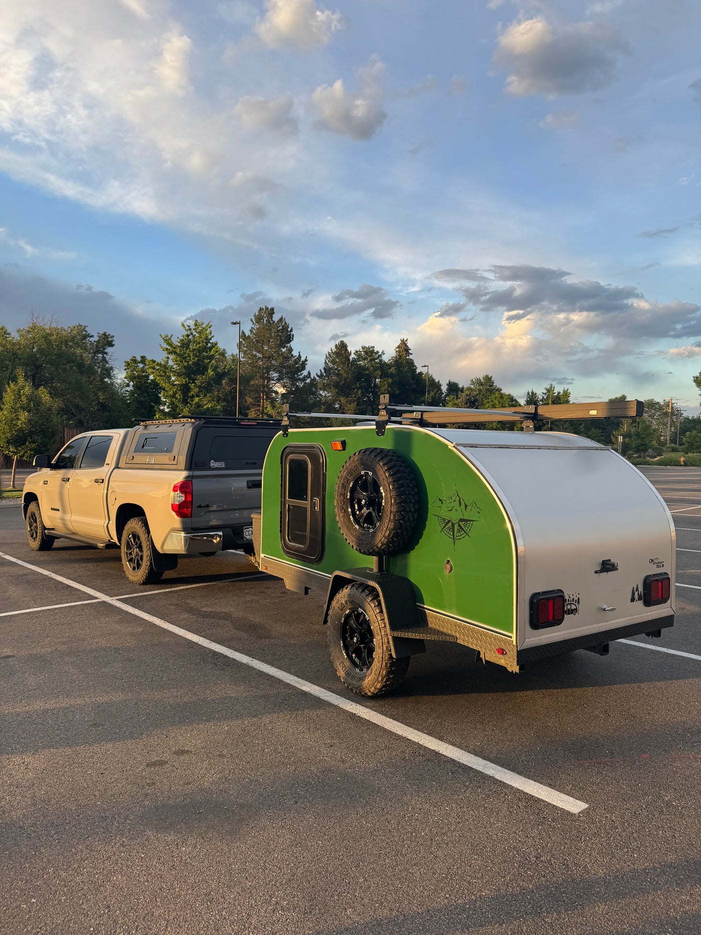Adventure-ready RV rental: Tan pickup truck with camper shell towing a green teardrop trailer, perfect for camping adventures under a cloudy sky.