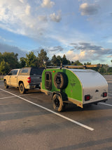 Adventure-ready RV rental: Tan pickup truck with camper shell towing a green teardrop trailer, perfect for camping adventures under a cloudy sky.