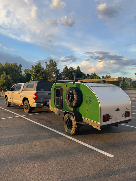 Adventure-ready RV rental: Tan pickup truck with camper shell towing a green teardrop trailer, perfect for camping adventures under a cloudy sky.