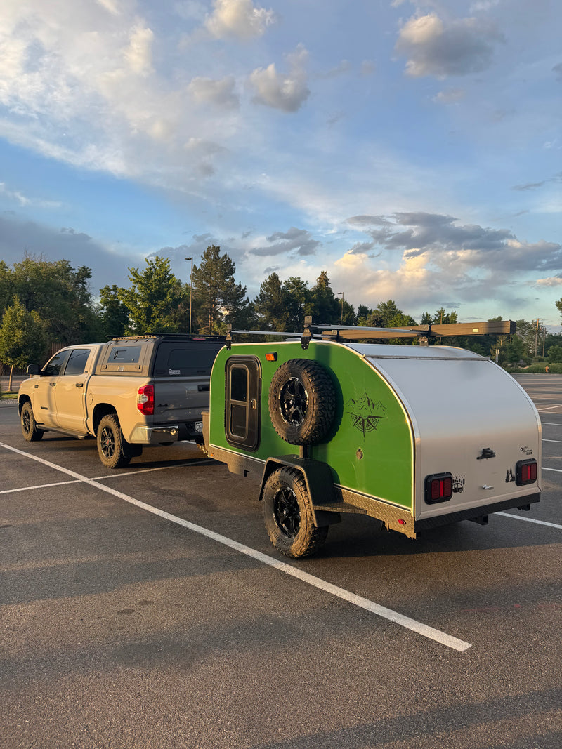 Adventure-ready RV rental: Tan pickup truck with camper shell towing a green teardrop trailer, perfect for camping adventures under a cloudy sky. — photo 1