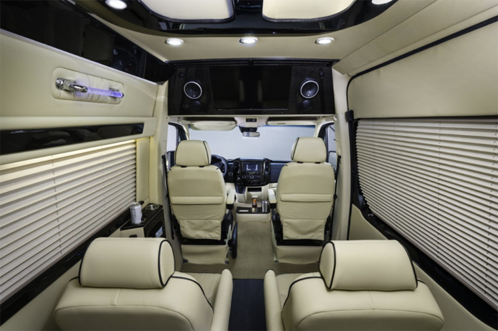 Luxurious RV rental interior: comfortable cream leather seating, entertainment screen, window blinds, and ambient lighting.