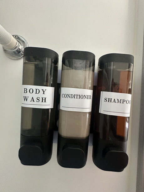 RV rental shower amenities: three labeled pump dispensers for body wash, conditioner, and shampoo on the wall.