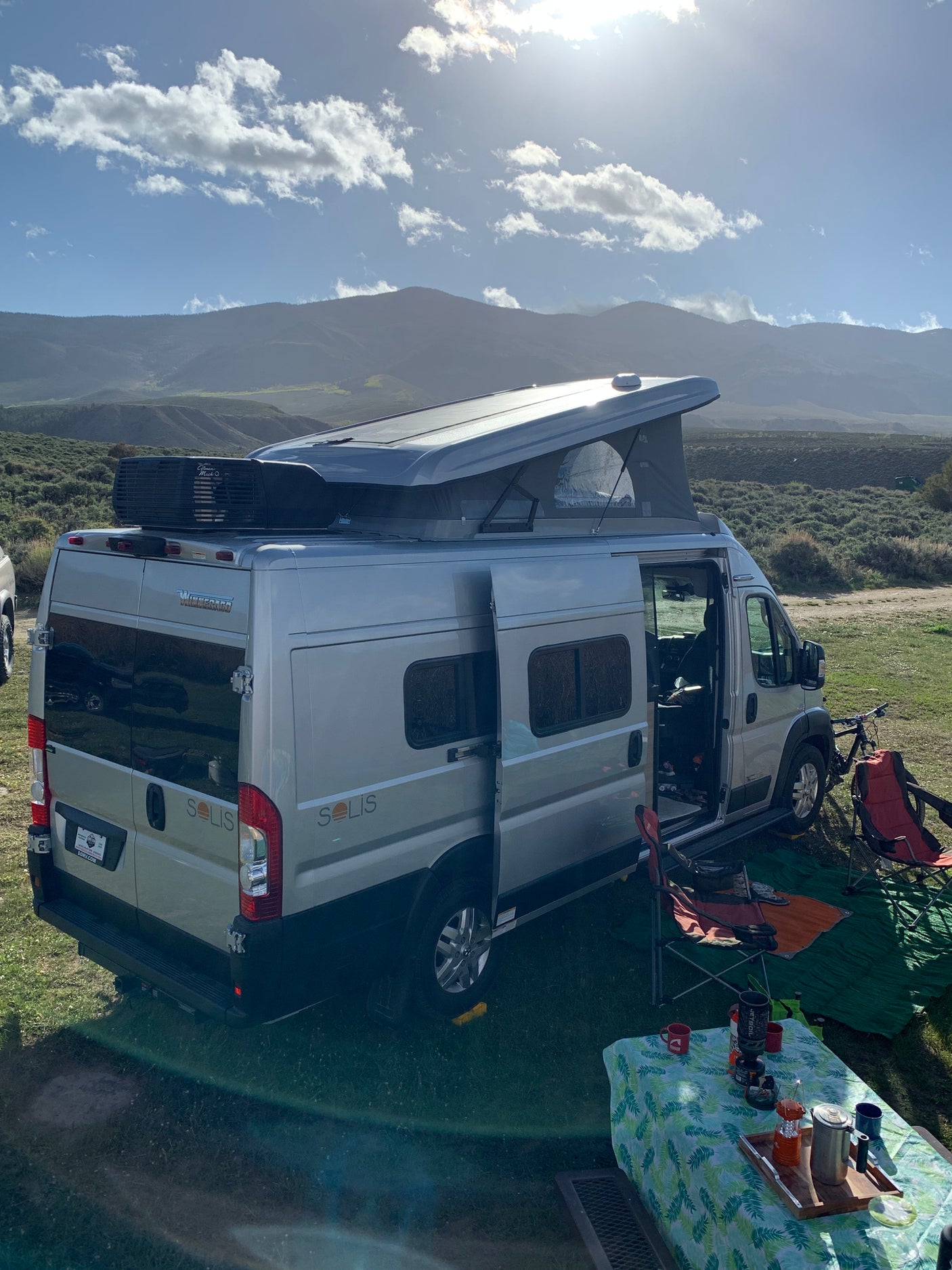 Winnebago Solis rv rental setup for camping, featuring an open pop-top & outdoor gear against a scenic mountain backdrop.