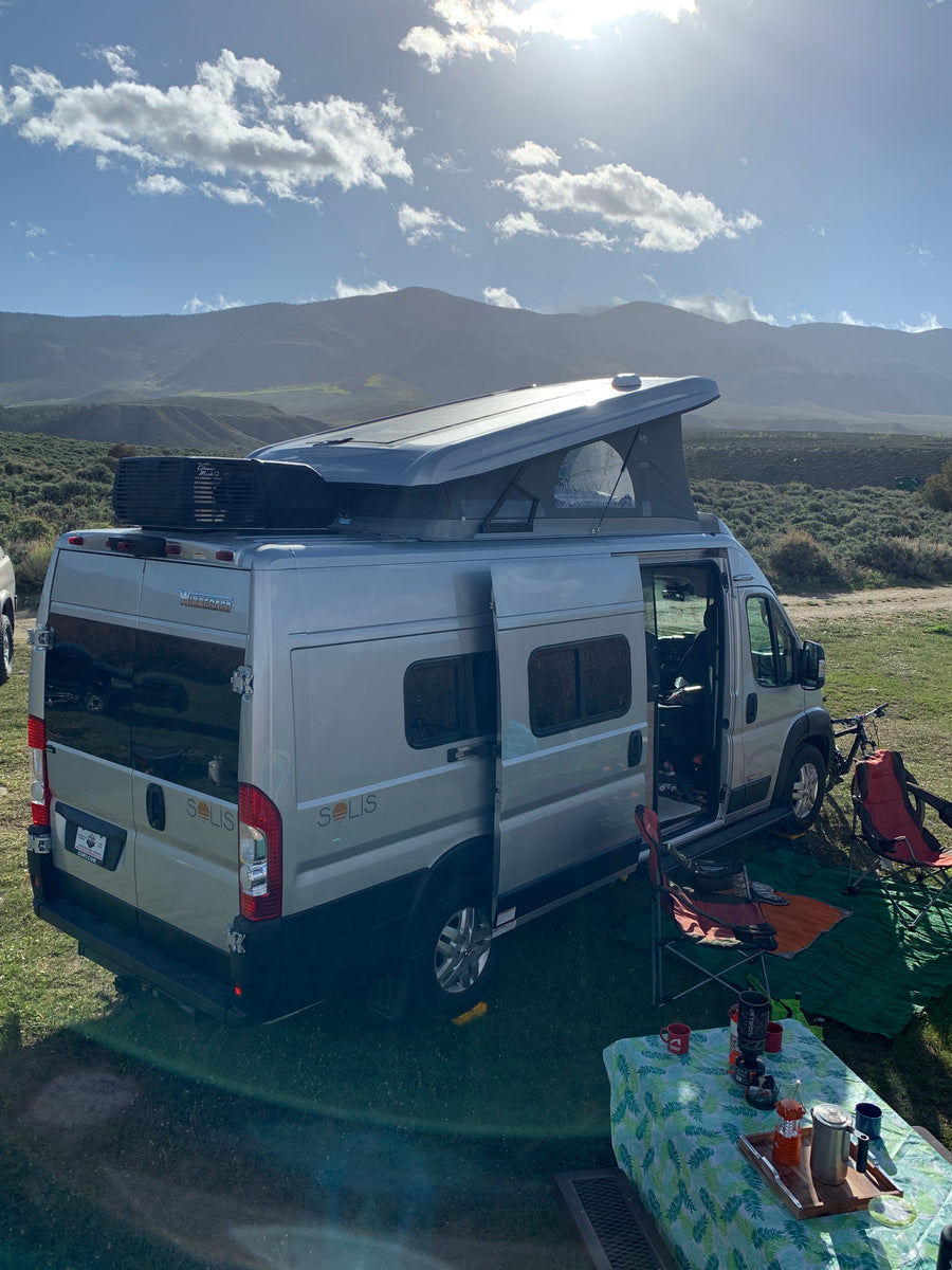 Winnebago Solis rv rental setup for camping, featuring an open pop-top & outdoor gear against a scenic mountain backdrop.