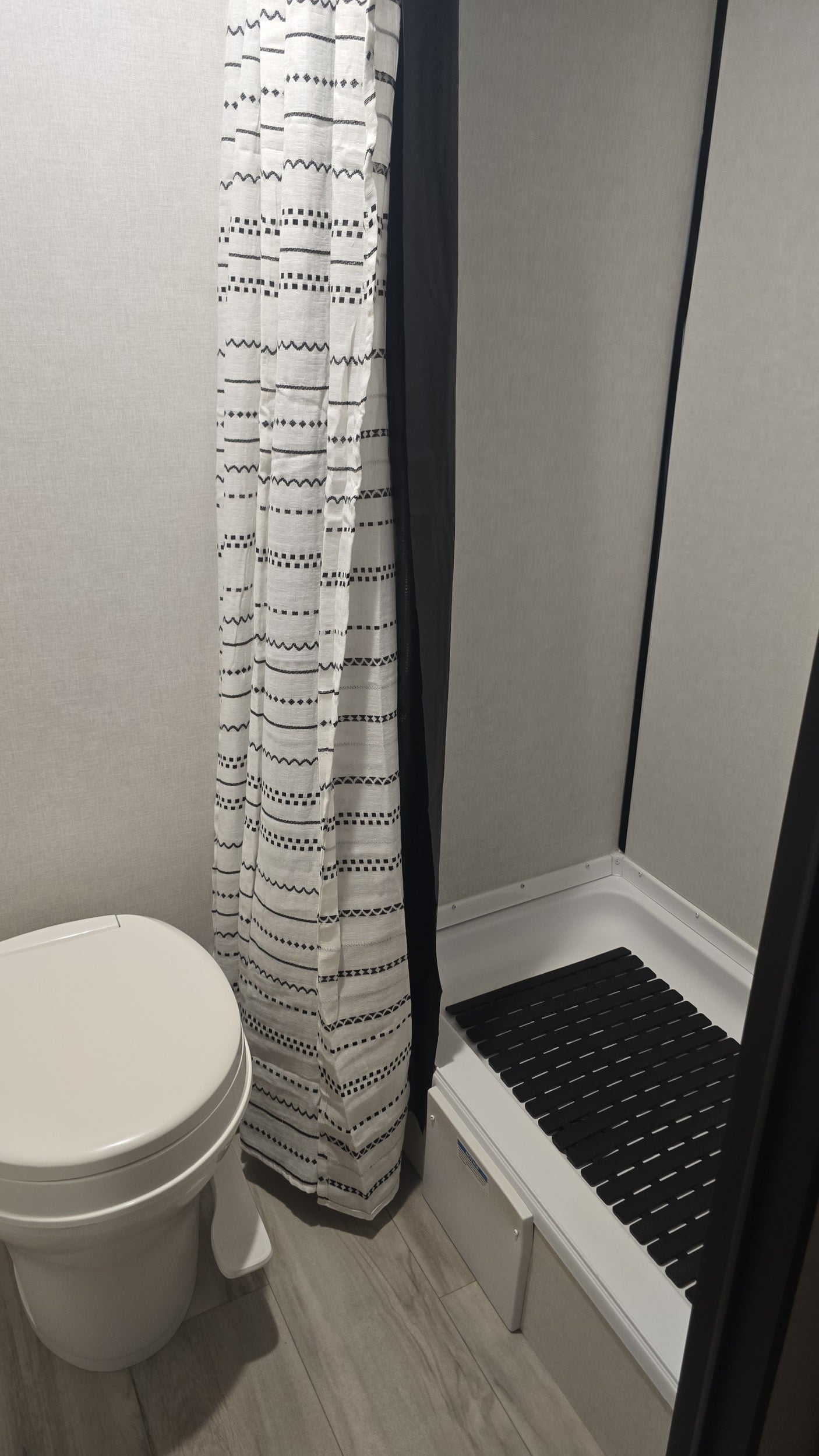 Compact RV rental bathroom: features a white toilet, patterned shower curtain, and shower stall with a black mat.
