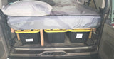 Efficient car camping setup in an RV rental with an elevated bed and labeled storage bins for gear.