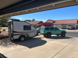 Teal Jeep with kayak, towing a white Grand Ascape travel trailer. This RV rental setup is parked in a sunny driveway.