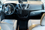 RV rental cabin: A functional Ford Transit dashboard with steering wheel, gear shifter, radio, and HVAC controls. Light gray seats.