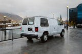 Explore with an rv rental! White van parked on wet street with city buildings, cloudy mountains, and streetlights.