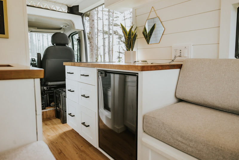 RV rental interior features a compact kitchen, cozy seating area with nature views, and modern finishes. — photo 8