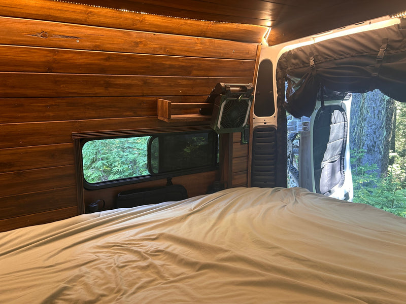 Cozy RV rental interior: a comfy bed, warm wooden walls with LED lights, a fan, and a lush forest view out the window. — photo 14