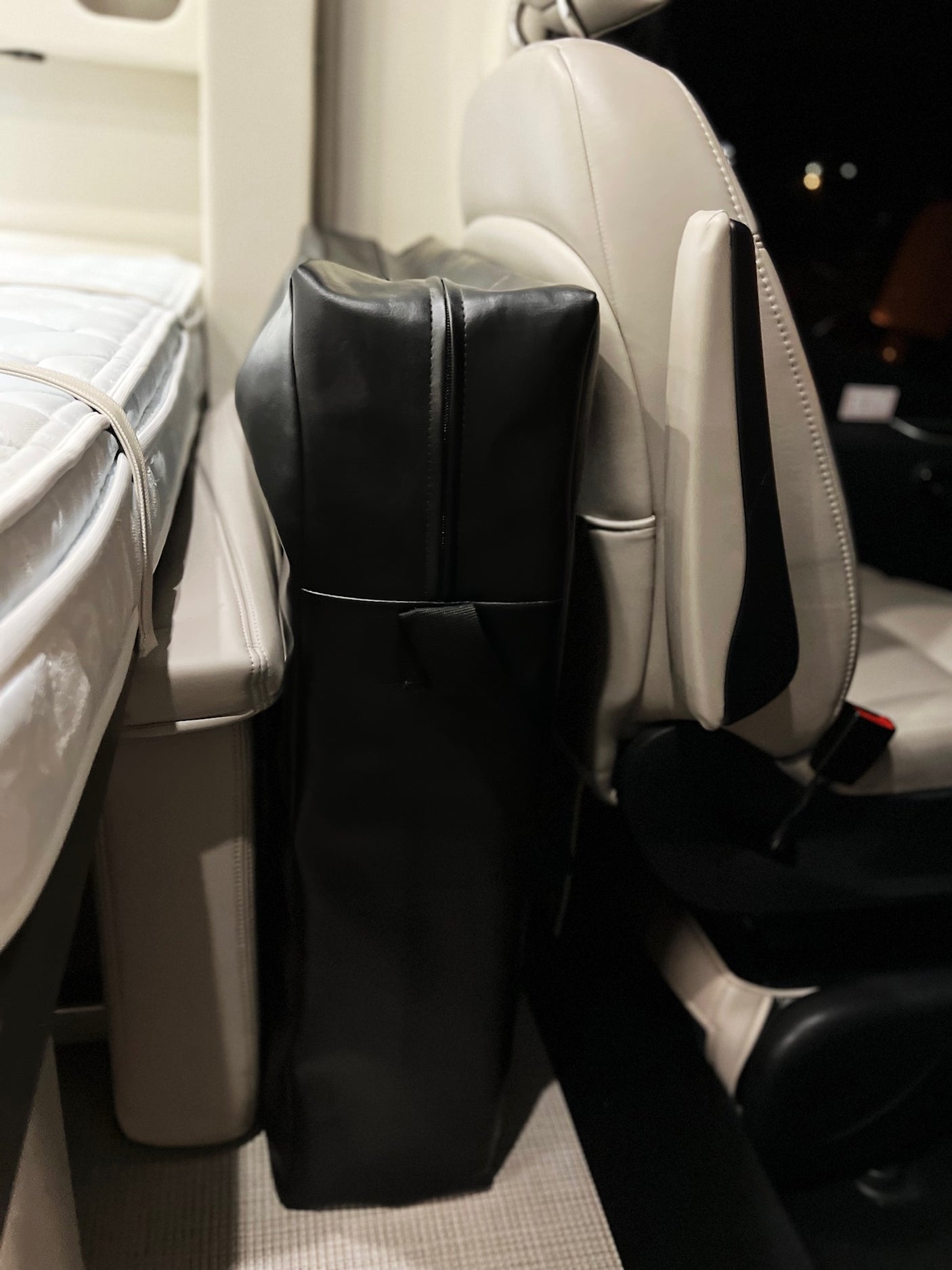 RV rental interior: A cozy bed with white mattress, a black standing luggage bag, and a light-colored passenger seat, ready for adventures.