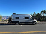 This silver RV rental, equipped with bikes, overlooks the Grand Canyon on a sunny day.