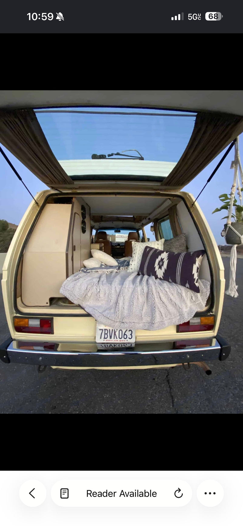 Inside a cozy vintage camper van RV rental, the open tailgate reveals a bed with patterned pillows, storage, and a hanging plant. — photo 3
