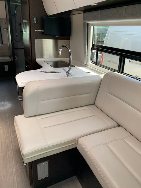 Explore this RV rental's sleek interior: compact kitchen, sink, TV, and comfy white leather seating.