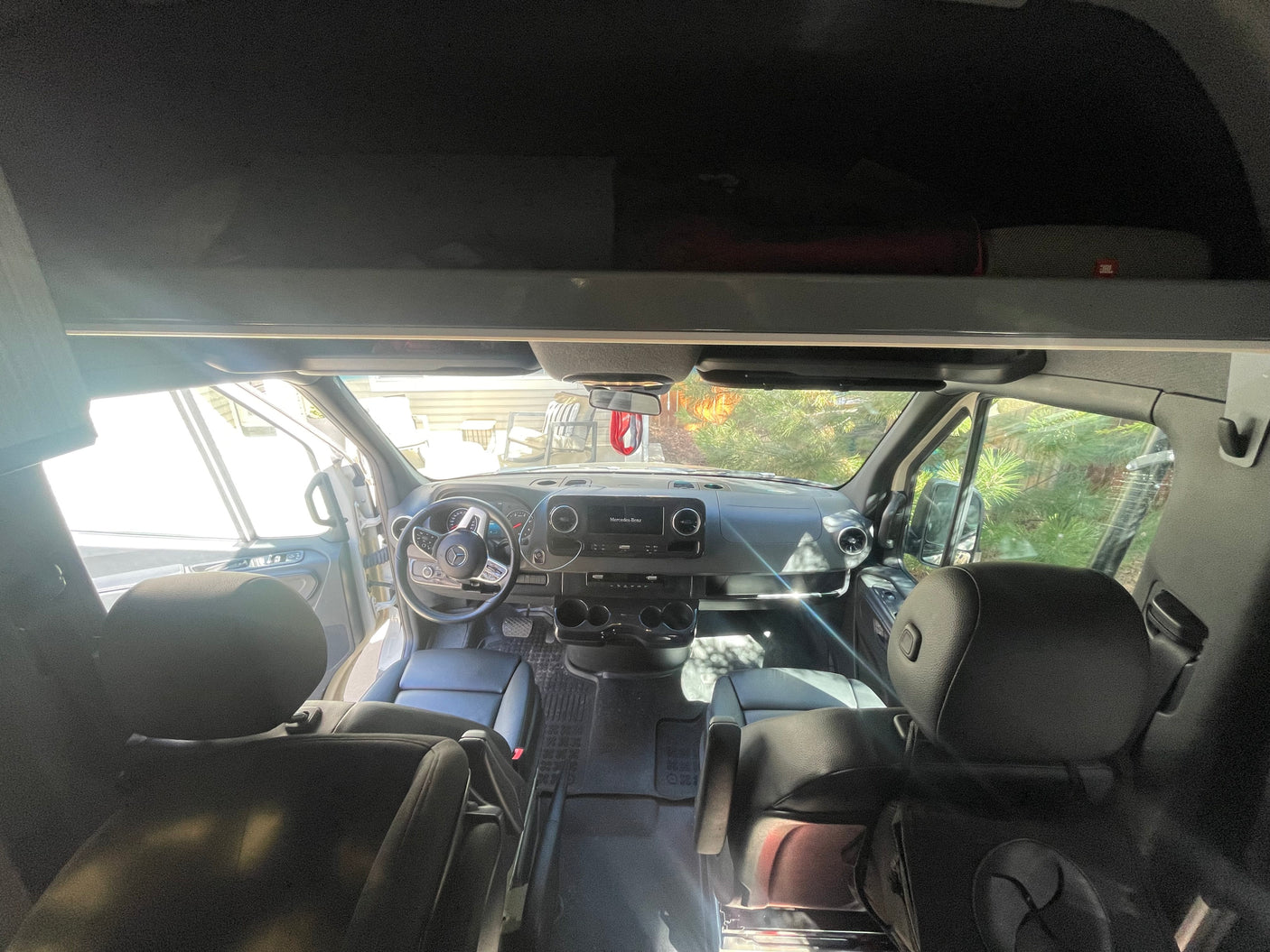 Interior view of an RV rental: front cabin with steering wheel, dashboard, and black leather seats, bright light from outside.