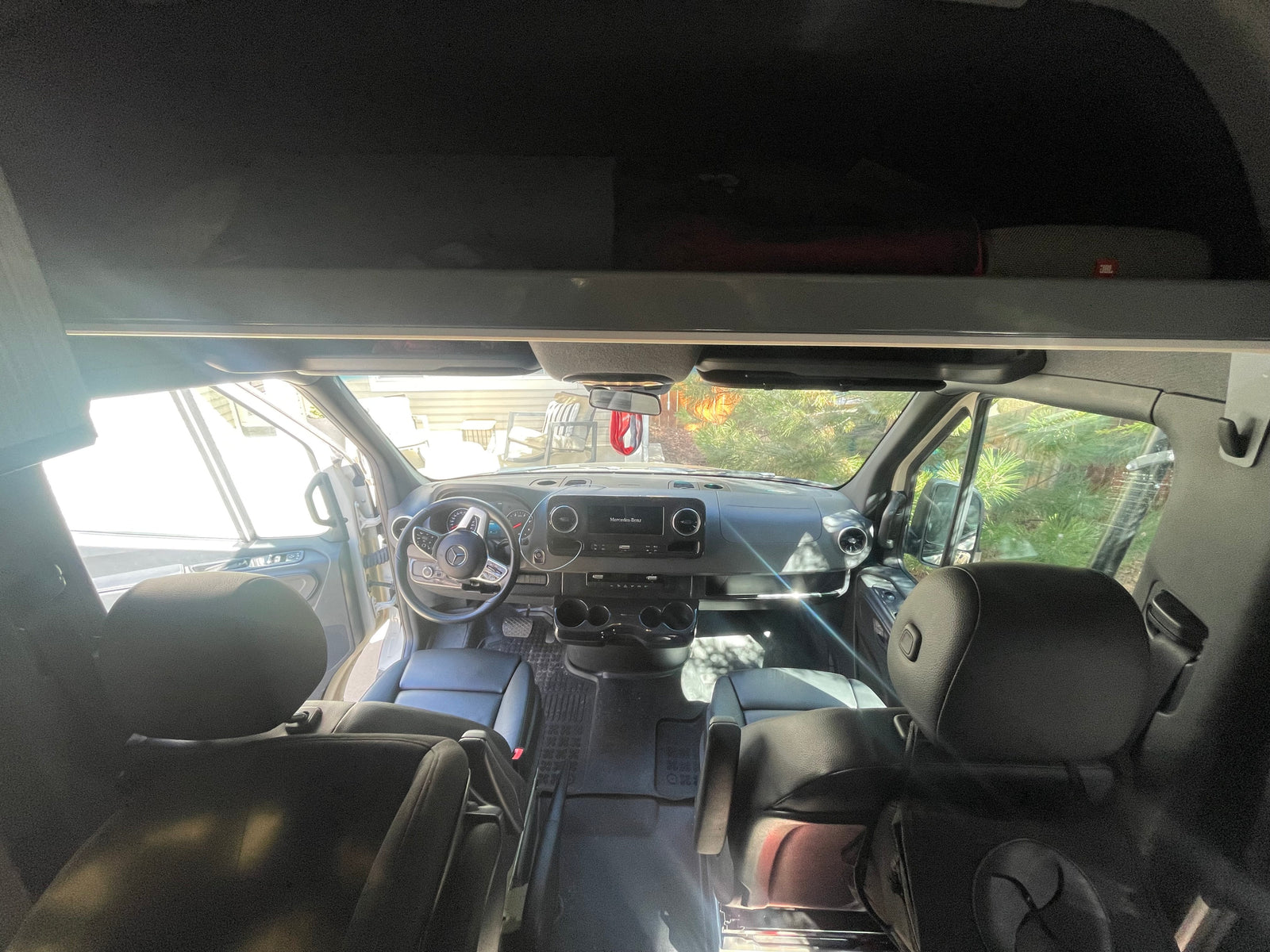 Interior view of an RV rental: front cabin with steering wheel, dashboard, and black leather seats, bright light from outside.