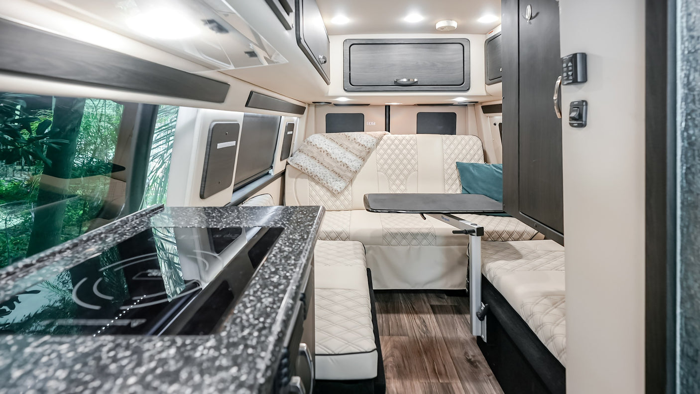 Modern RV rental interior: kitchen with stove, versatile living area, and large windows with green views.