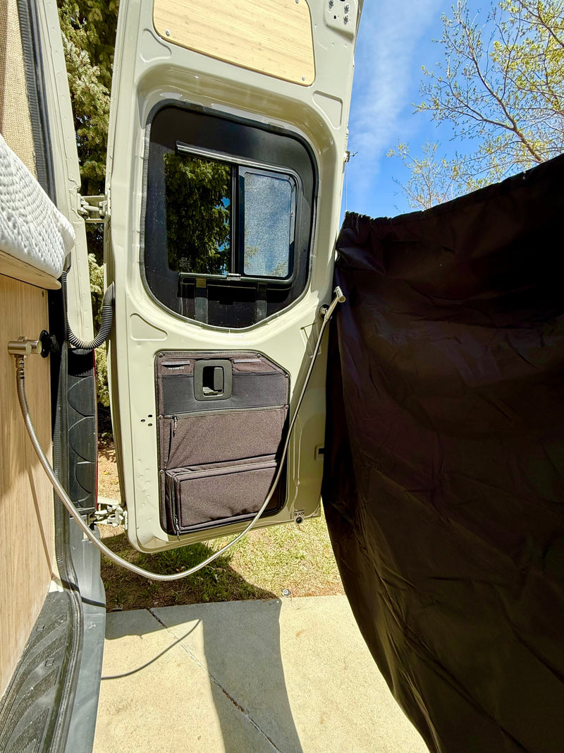 This RV rental detail shows a van's rear door open with built-in storage and an outdoor shower privacy curtain setup. — photo 9