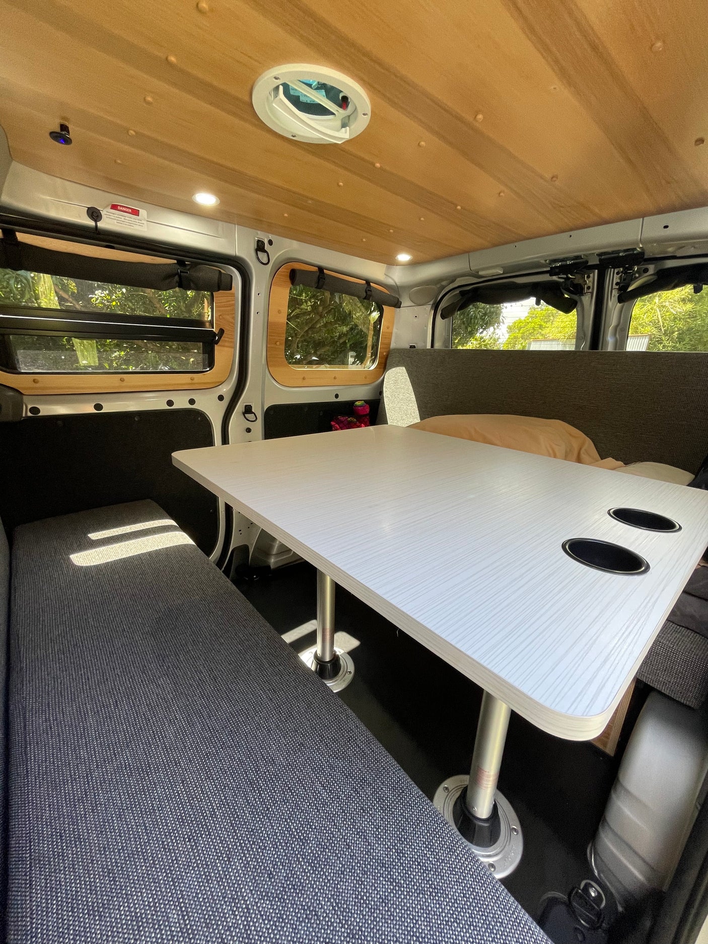 This RV rental's spacious interior features a bright dining table with cup holders, comfy gray benches, and wood-paneled ceiling.