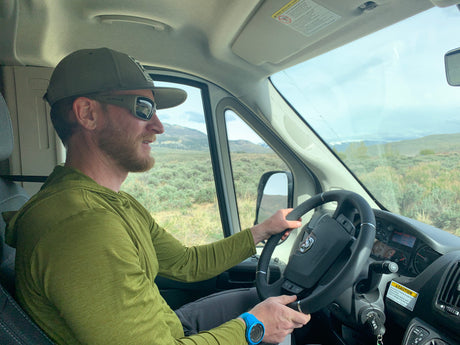 Man in Native sunglasses and hat, driving an RV rental. Scenic outdoor journey through open landscapes.