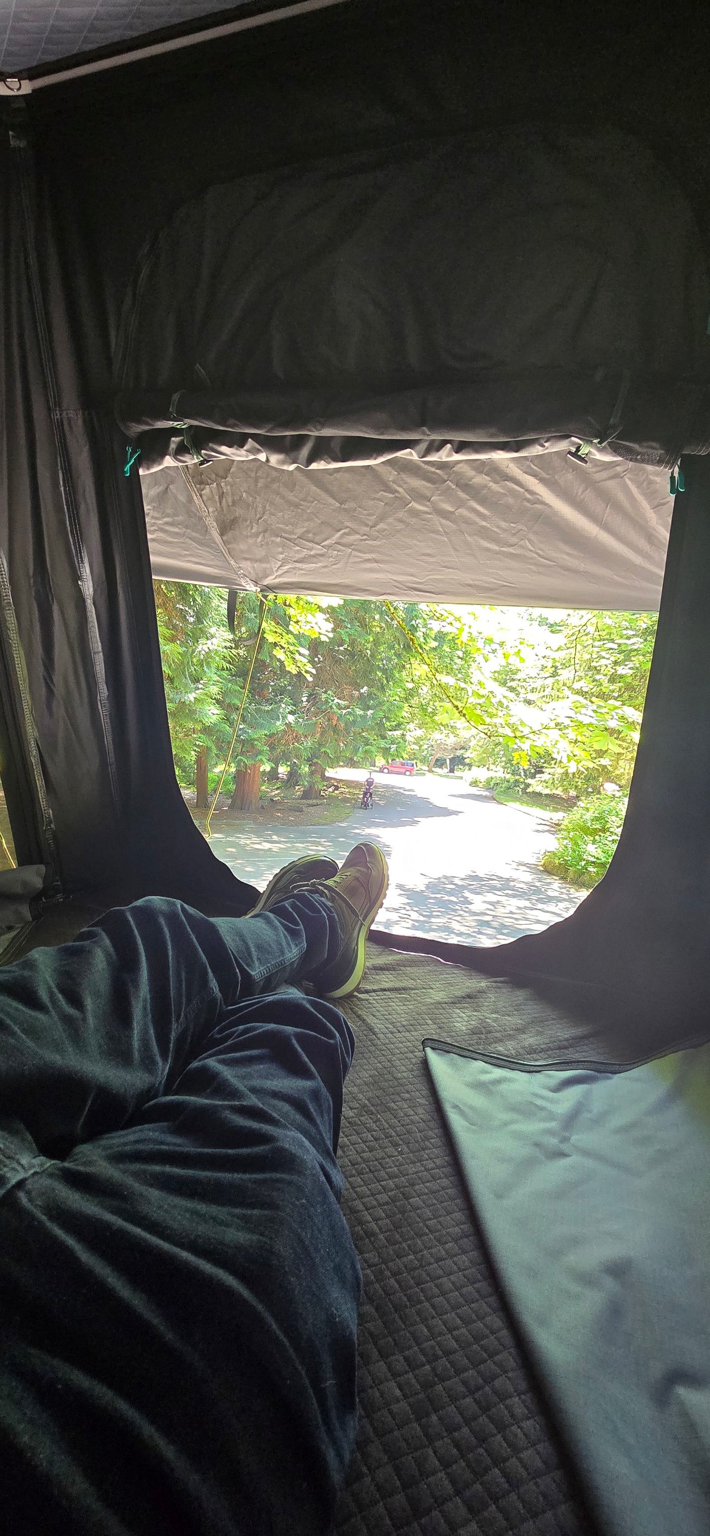 Legs stretched out in an RV rental, gazing at the sunlit road & green trees. Relaxing outdoor escape.