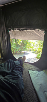 Legs stretched out in an RV rental, gazing at the sunlit road & green trees. Relaxing outdoor escape.