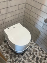 Compact Thetford portable toilet in a bright RV rental bathroom, featuring grey subway wall tiles and a pebble floor.