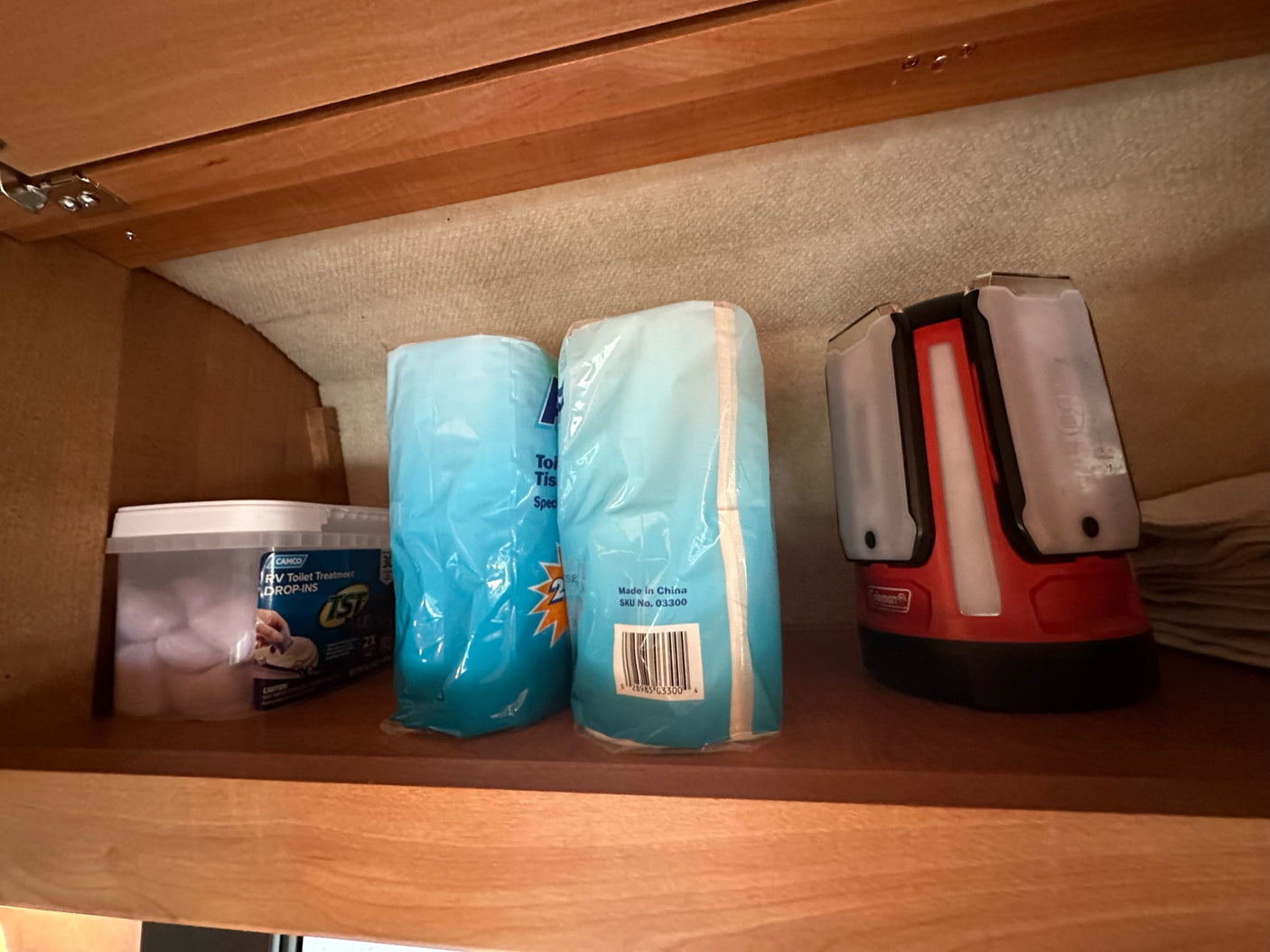 RV rental cabinet with essential supplies: toilet paper, RV toilet treatment, and a Coleman lantern, neatly organized.