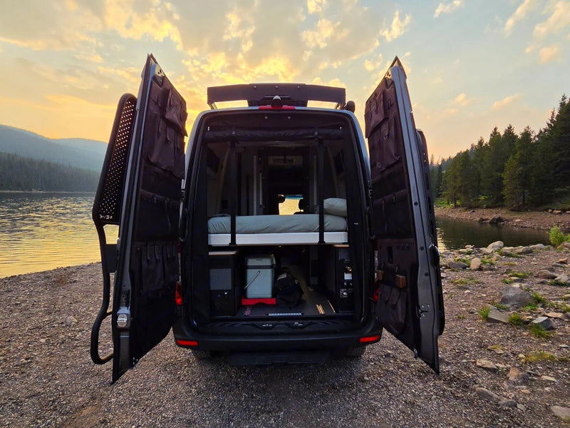  parked on a dirt road by trees. Ready for adventure!|Experience van life with an RV rental! Camper van doors open to a serene lake at sunset — photo 6