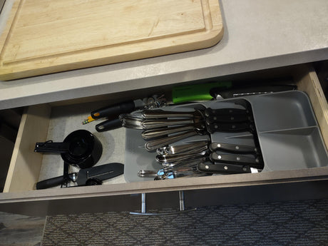 RV rental kitchen drawer, neatly organized with cooking utensils, flatware, knives, and measuring cups. Cutting board above.