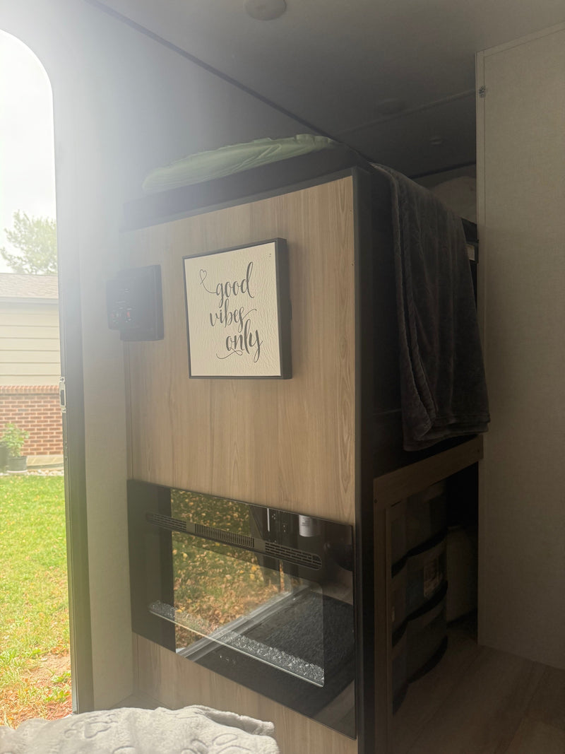 RV rental interior featuring a "good vibes only" sign, control panel, and electric fireplace, with a view of the yard. — photo 5