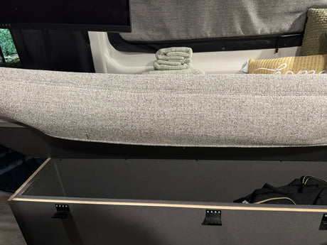 Cozy RV rental interior: gray seating, green towels, yellow pillow, and practical under-seat storage with a black bag.