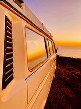 A white RV rental enjoys a stunning sunset view by the ocean. Perfect for coastal van life adventures.