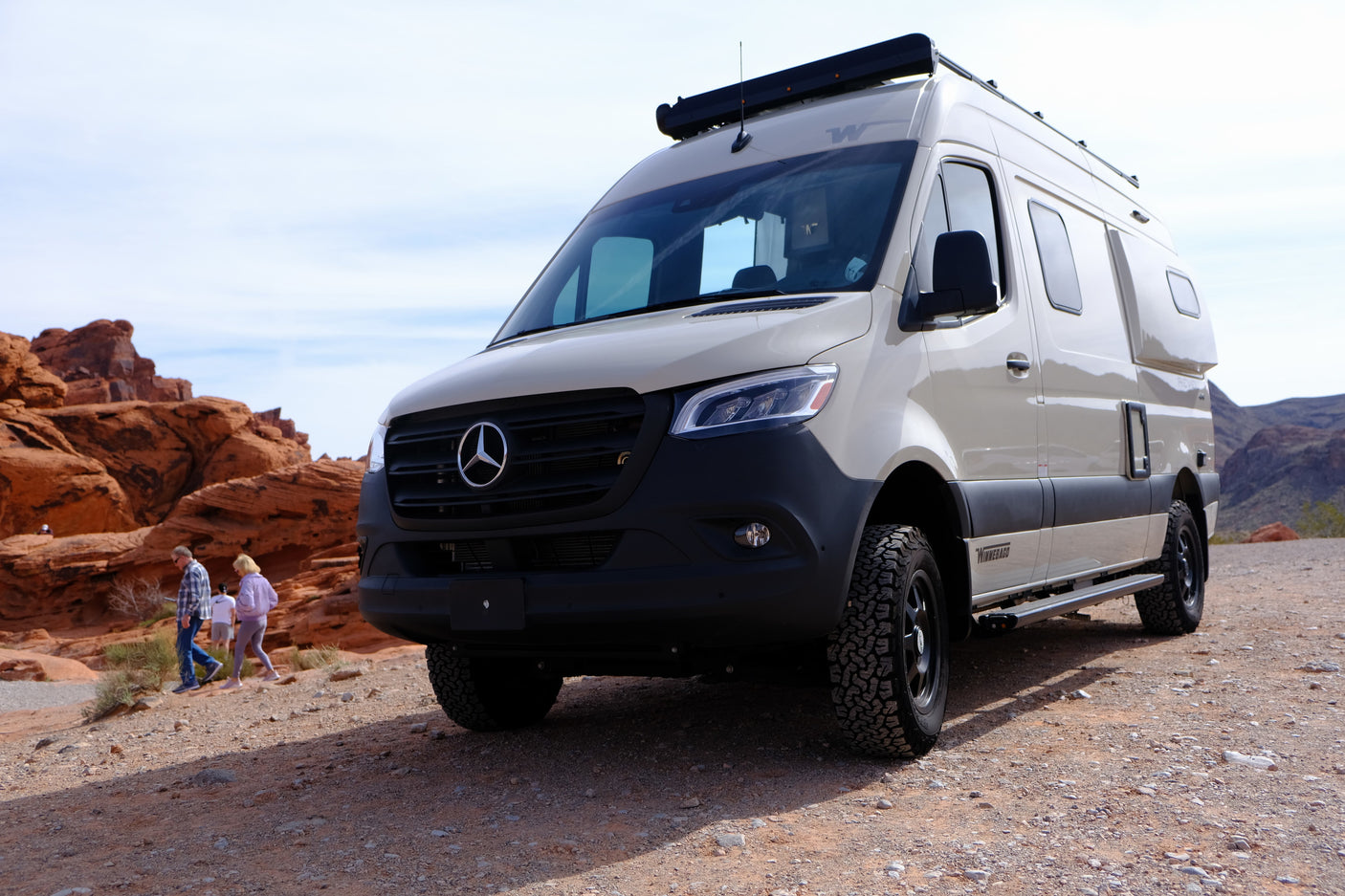 Winnebago Mercedes-Benz Sprinter RV rental on a dirt road in a red rock desert. People walk nearby, enjoying the views.
