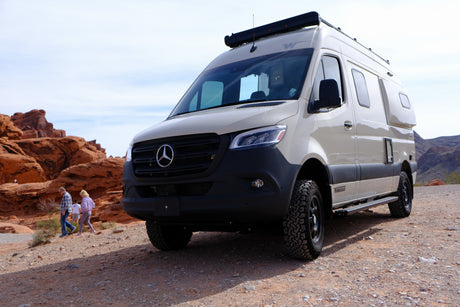 Winnebago Mercedes-Benz Sprinter RV rental on a dirt road in a red rock desert. People walk nearby, enjoying the views.