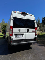 Rear of a white Ram ProMaster rv rental camper van, parked outdoors on a sunny day with a crescent moon in the blue sky.