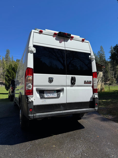 Rear of a white Ram ProMaster rv rental camper van, parked outdoors on a sunny day with a crescent moon in the blue sky.
