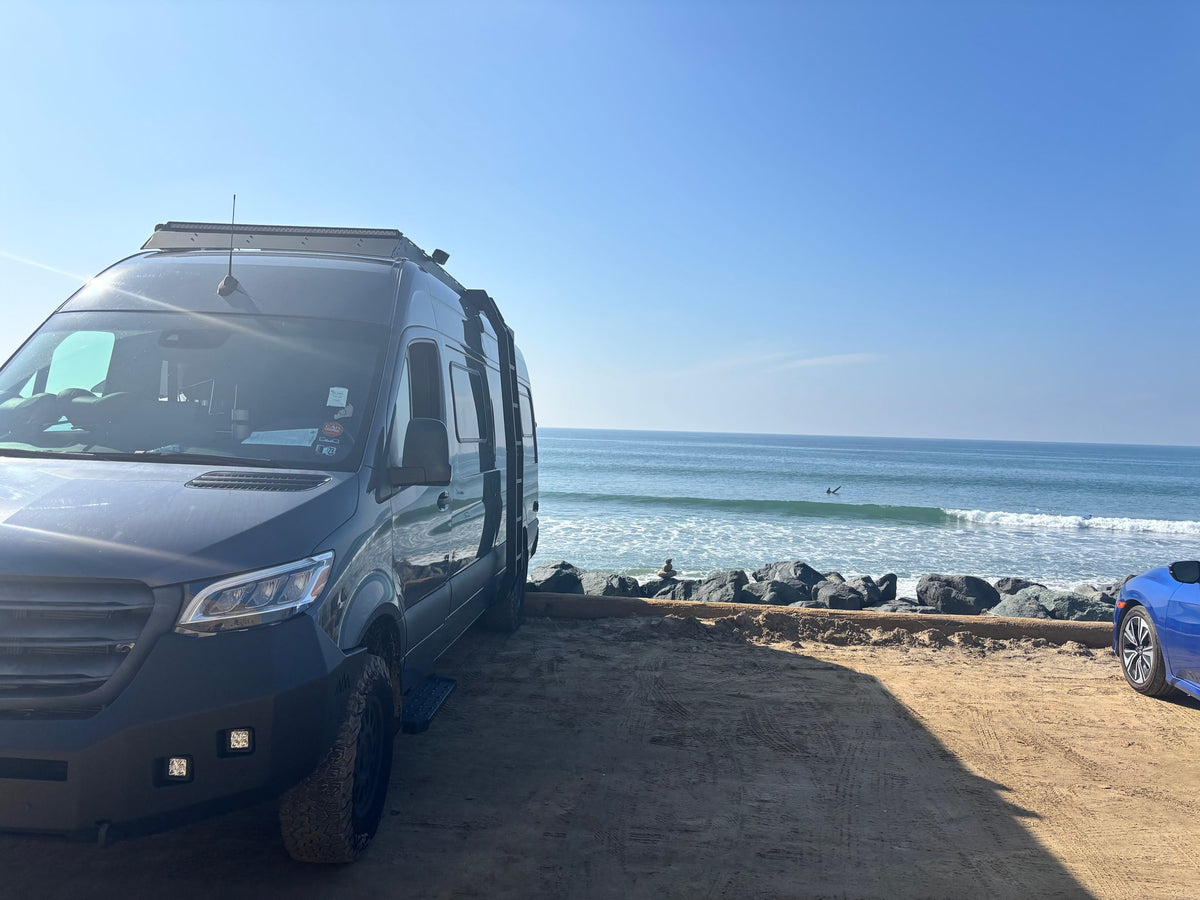 Coastal rv rental: Dark camper van parked on a sandy beach. Ocean waves