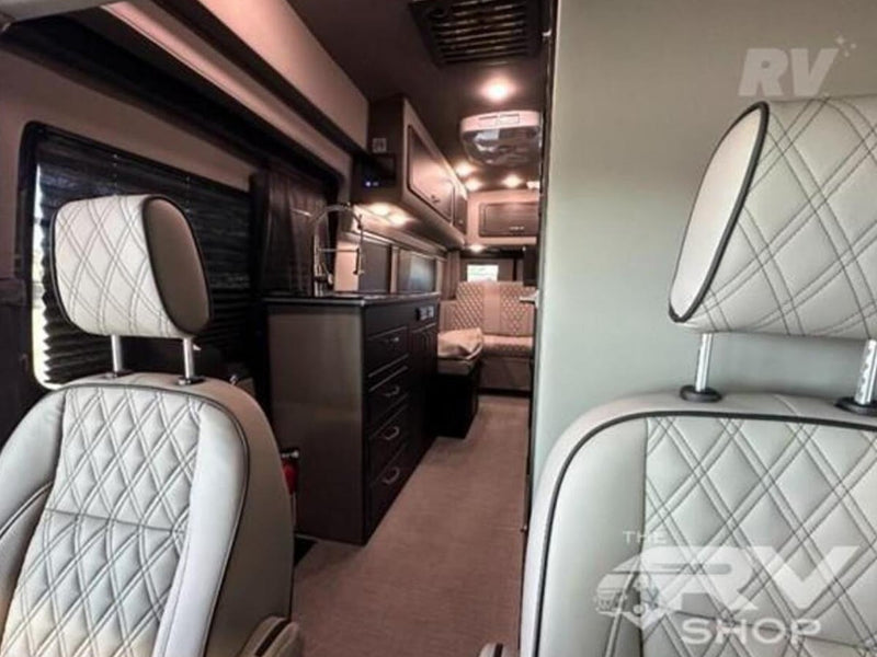  parked at an RV shop under a clear sky.|Gray camper van with awning & tinted windows. Ready for rv rental from The RV Shop.|Comfortable RV rental interior: Detailed view of a camper van's stylish quilted front seats — photo 7