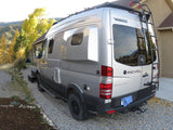 A silver Winnebago Revel 4x4 Mercedes Sprinter camper van on a gravel driveway. Consider this for your rv rental.