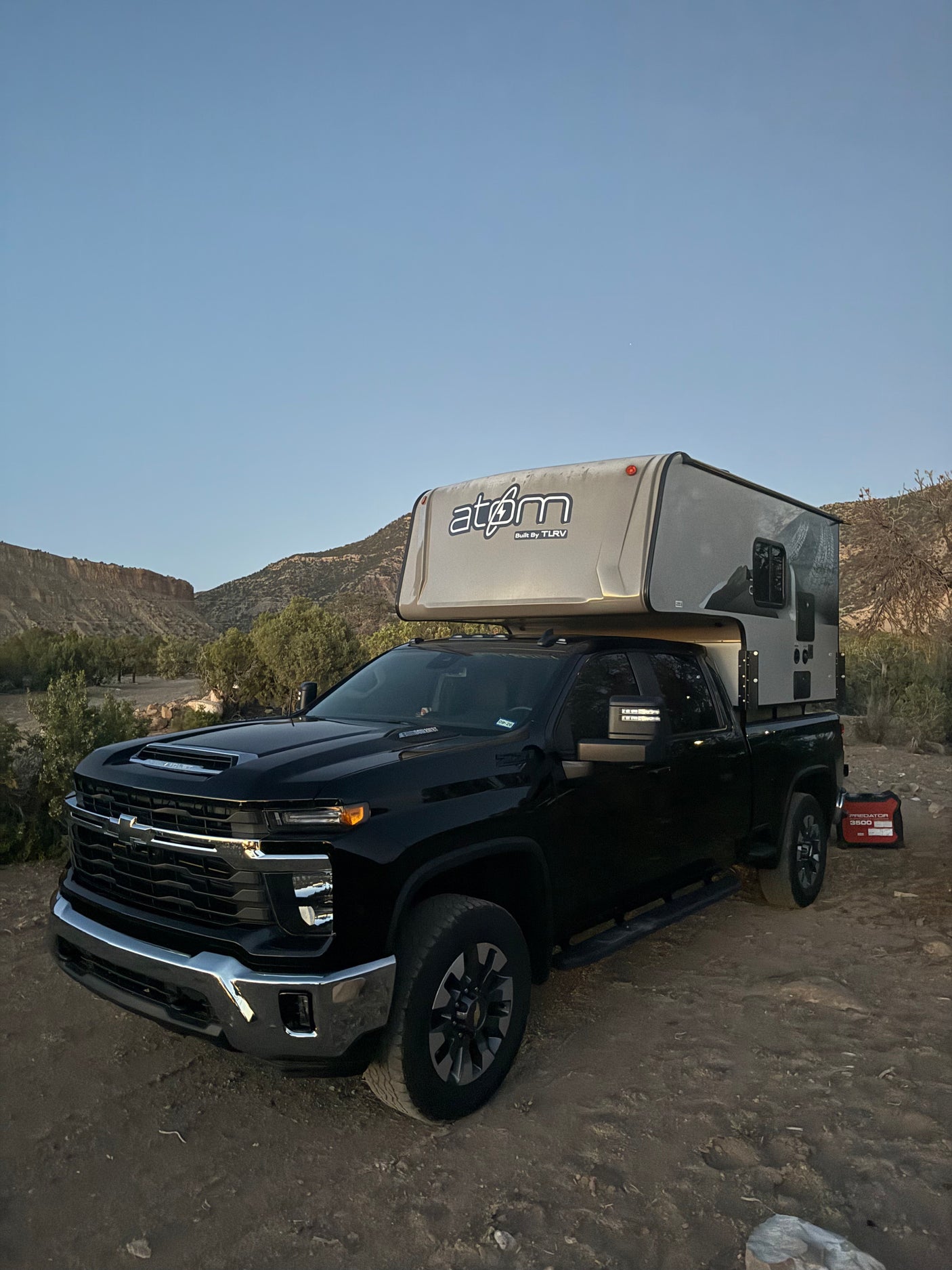 A black Chevrolet pickup truck with an Atom truck camper, ready for rugged RV rental and overland camping adventures.
