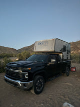 A black Chevrolet pickup truck with an Atom truck camper, ready for rugged RV rental and overland camping adventures.