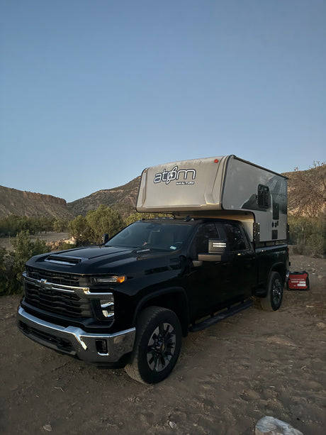 A black Chevrolet pickup truck with an Atom truck camper, ready for rugged RV rental and overland camping adventures.