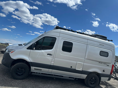 Explore with this bright Winnebago Revel 4x4 camper van rv rental. Parked outdoors with a bike rack under a blue, cloudy sky.