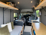Cozy RV rental camper van interior with bed, Dometic fridge, kitchen sink, wooden shelving, and front seats visible.