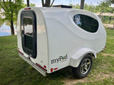 Compact white myPod travel trailer, great for an RV rental, parked by a river with trees. Perfect for camping trips.