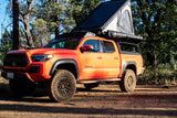 Vibrant orange Toyota Tacoma with an open rooftop tent, perfect for an off-road RV rental camping adventure in the forest.